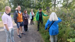 Ryhmä ihmisiä seisoo kesäisellä polulla, yksi ihmisistä näyttää esittelevän jotain kasvia muille.