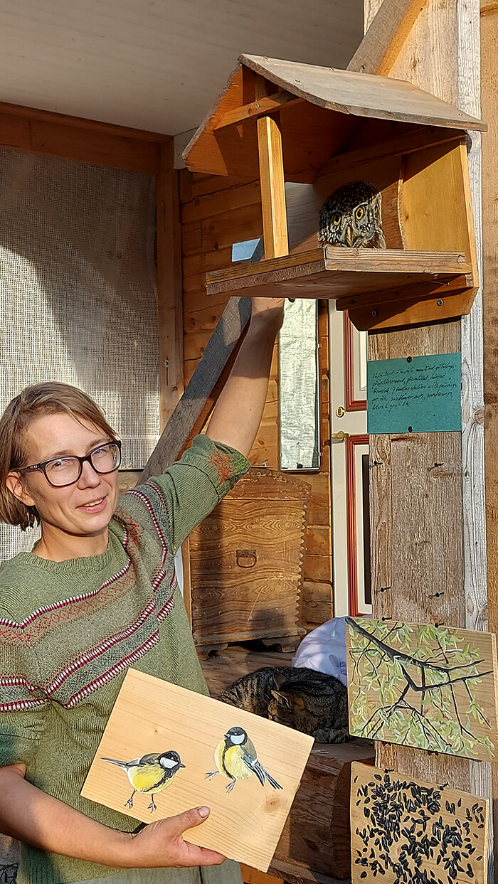 Taiteilija Jane Remm pitelee levyä, jossa on maalattuja lintuja, kuvattuna sisätiloissa.