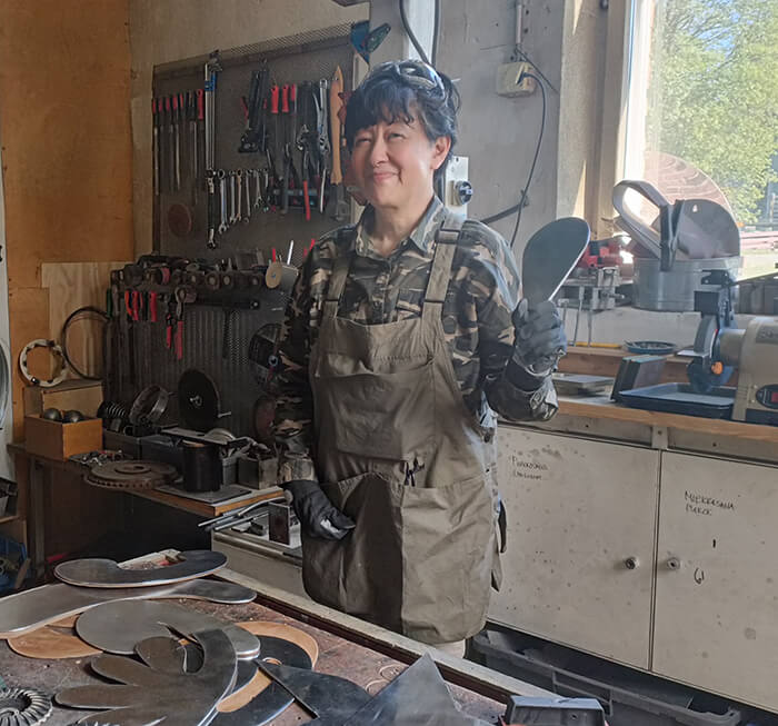 Taiteilija Masami Aihara seisoo työpajassa ja hymyilee.